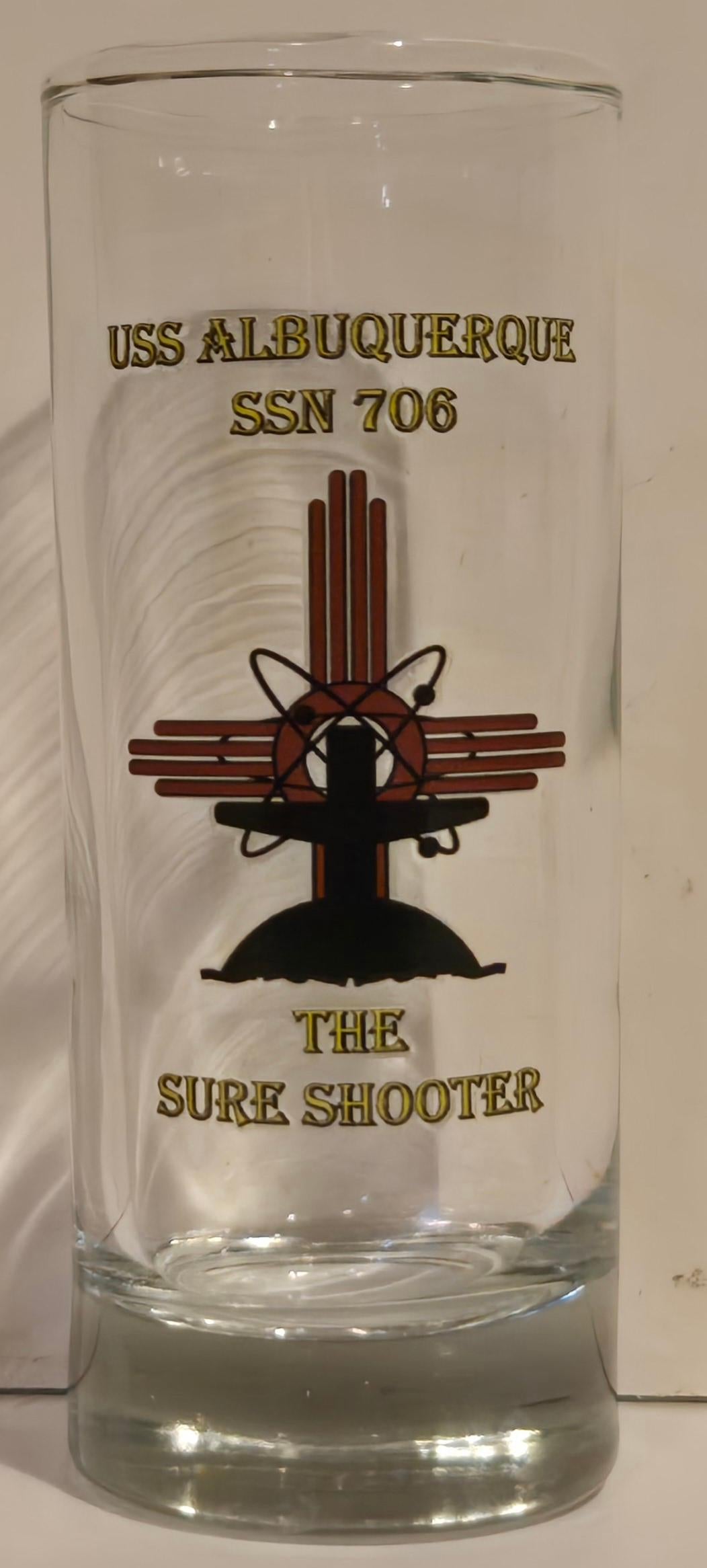 A clear glass shot glass with the text 'USS ALBUQUERQUE SSN 706' and 'THE SURF SHOOTER' along with a graphic design of a submarine.